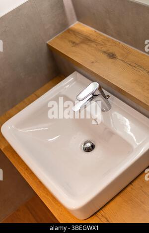 Dieses Badezimmer verfügt über ein kompaktes, modernes Waschbecken mit einem eleganten Chrom-Wasserhahn, der auf einer Holzarbeitsfläche sitzt. Das minimalistische Design ergänzt den Stockfoto