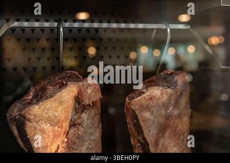 Zwei Fleischstücke hängen in einem Restaurant, beleuchtet durch sanfte Beleuchtung. Das Ambiente ist einladend und unterstreicht die Qualität der ausgestellten Fleischsorten Stockfoto