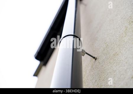Nahaufnahme des schwarzen fallauswurfrohrs, das an einer Hauswand mit weißer Fassade und Montagehalterung befestigt ist Stockfoto