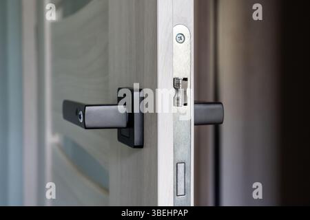 Nahaufnahme eines modernen schwarzen Türgriffs an einer leicht geöffneten Innentür aus Holz mit Metallverriegelungsmechanismus, minimalistisches Design für die Sicherheit des Hauses Stockfoto