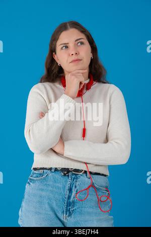 Eine nachdenkliche junge Frau mit Kopfhörern, die gegen Blau schaut Stockfoto