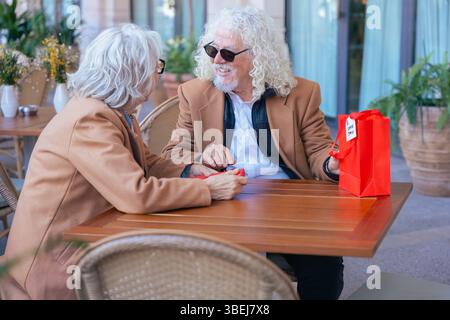 Lächelndes Seniorenpaar genießt gemeinsam Kaffee im Café im Freien in lässigen Outfits Stockfoto