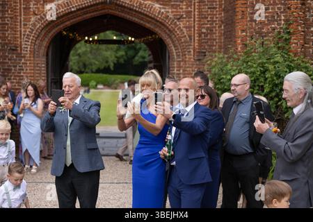 Gast bei der Hochzeit, der Fotos mit dem Mobiltelefon der Braut und des Bräutigams macht. Stockfoto
