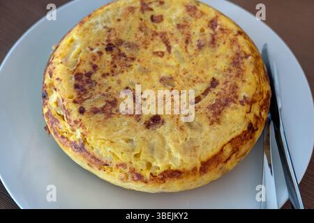 Hausgemachte ganze Tortilla auf einem Tisch, goldbraunes Omelett mit Eiern, dünn geschnittenen Kartoffeln und süßen Zwiebeln, die die reichhaltige Textur zeigen Stockfoto