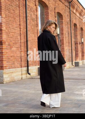 Frau im lässigen Streetstyle-Mantel genießt einen sonnigen Tag in der Stadt Stockfoto
