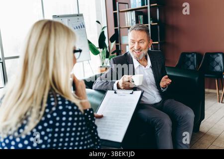 Professionelles Geschäftstreffen in einem modernen Büro mit zwei Führungskräften, die in einer entspannten und kollaborativen Umgebung über die Arbeit bei Kaffee diskutieren Stockfoto