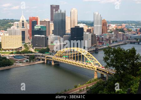 Pittsburgh, Pennsylvania, USA - 8. August 2023: Die Skyline von Pittsburgh zeigt moderne Gebäude neben einer lebhaften gelben Brücke. Stockfoto