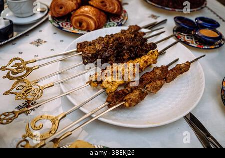 Verschiedene gegrillte Fleischspieße auf traditionellem Tisch mit dekorativen Tellern Mai 29,2025 Stockfoto