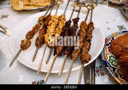 Verschiedene gegrillte Fleischspieße auf traditionellem Tisch mit dekorativen Tellern Mai 29,2025 Stockfoto