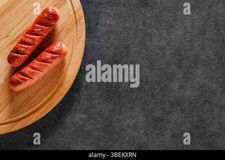 Zwei gegrillte Würstchen auf Holzbrett auf dunkler Arbeitsplatte, Blick von oben Stockfoto