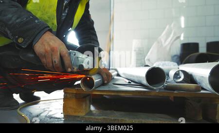 Arbeiter, der Metallrohre mit Winkelschleifer schneidet. Eine Nahaufnahme eines Arbeiters mit einem Winkelschleifer, um ein Metallrohr zu schneiden, mit leuchtenden Funken, die in alle hineinfliegen Stockfoto