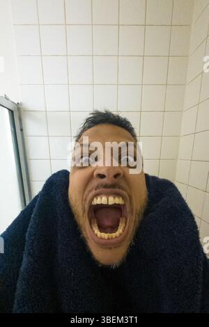 Ein Mann mit einem großen Lächeln im Gesicht und weit geöffnetem Mund. Er trägt ein blaues Handtuch Stockfoto
