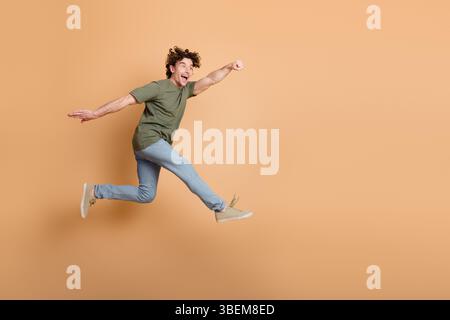 Junger Mann in lässigem Outfit, der fröhlich mit einem fröhlichen Lächeln auf beigefarbenem Hintergrund springt und Glück ausdrückt Stockfoto