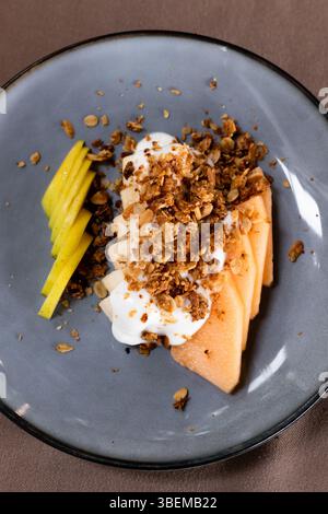 Nahaufnahme eines wunderschön präsentierten mexikanischen Desserts mit Mangoblättern mit Joghurt und Müsli auf einer strukturierten Keramikplatte, o Stockfoto