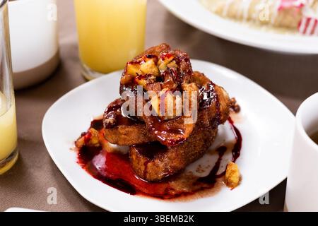 Eine Nahaufnahme eines Tellers französischen Toast, garniert mit gehackten Früchten und einer lebendigen Beerensauce, serviert mit einem Glas Orangensaft und Stockfoto