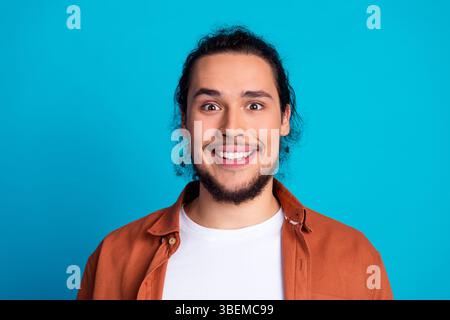 Porträt eines jungen Mannes mit einem fröhlichen Ausdruck vor einem leuchtend blauen Hintergrund, der ein lässiges oranges Hemd trägt. Stockfoto