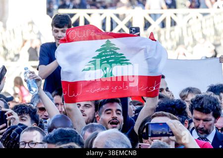 Vatikanstadt, 8. Mai 2025. Ein Gläubiger hält eine libanesische Flagge, während weißer Rauch aus dem Kamin auf der Spitze der Sixtinischen Kapelle austritt und damit die Wahl des neuen Papstes durch das Konklave signalisiert. Stockfoto