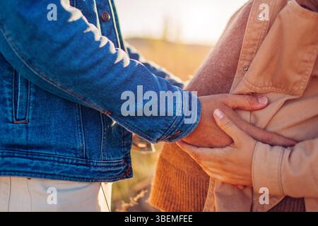 Der zukünftige Vater berührt den Bauch seiner Frau. Schwangere Familienpaare gehen bei Sonnenuntergang draußen. Zukünftige Eltern Stockfoto