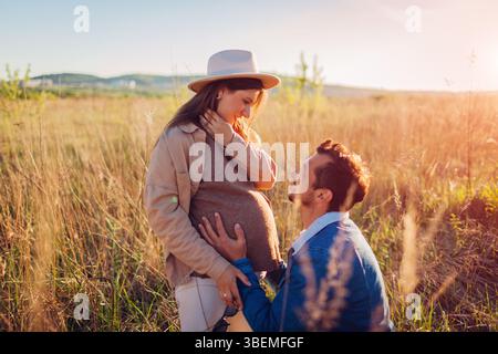 Ein junges schwangeres Familienpaar, das draußen läuft. Der zukünftige Vater berührt den Bauch seiner Frau. Stockfoto