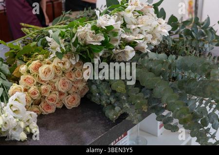 Eine Auswahl an frischen Blumen und Eukalyptuszweigen liegt auf dem Schreibtisch eines Blumenhandels mit weißer Alstroemeria, cremefarbenen Rosen und grünem Laub Stockfoto