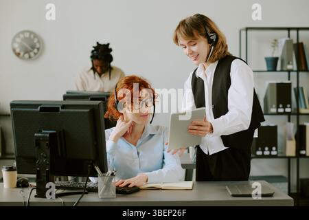 Nachwuchsexperten, die digitale Inhalte auf einem Tablet überprüfen, während sie in einer modernen Büroumgebung arbeiten. Durchdachte Atmosphäre mit verschiedenen Teammitgliedern Co Stockfoto