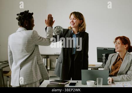 Eine Gruppe multikultureller Geschäftsfrauen feiert erfolgreiche Erfolge in modernen Büroumgebungen, zeigt Begeisterung und Kameradschaft während der Arbeit Stockfoto