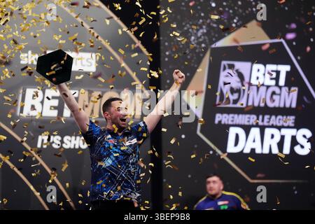 Luke Humphries feiert mit der Trophäe, nachdem er das Finale gegen Luke Litttler während der BetMGM Premier League Play-offs im O2, London gewonnen hat. Bilddatum: Donnerstag, 29. Mai 2025. Stockfoto