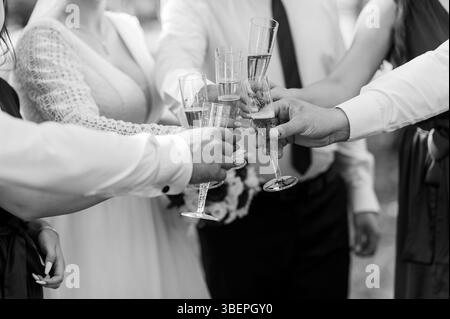 Eine fröhliche Schwarzweiß-Hochzeitsszene mit mehreren Personen, die Champagner in einem Toast hochheben, unter denen die Braut im Spitzenkleid zu sehen ist Stockfoto