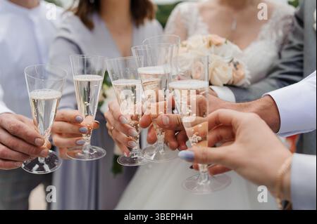 Ein fröhlicher Hochzeitstoast mit Sektgläsern, die unter elegant gekleideten Gästen gefeiert werden, mit Braut und Bräutigam als Mittelpunkt Stockfoto