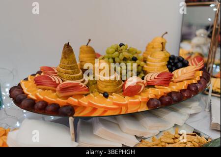 Auf einer wunderschön gestuften Servierplatte werden geschnittene Orangen, Äpfel, Birnen, Trauben, Brombeeren und andere Früchte präsentiert Stockfoto