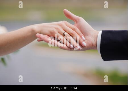 Nahaufnahme der Hände eines frisch verheirateten Paares, die während einer Feier im Freien ihre goldenen Eheringe zeigen, ein Symbol für Liebe, Engagement und einen SHA Stockfoto
