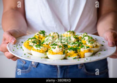 Eine Frau, die eine weiße Platte mit verfluchten Eiern hält, garniert mit Schnittlauch Stockfoto