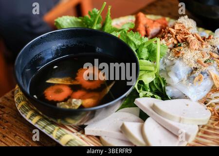 Banh Cuon nach Hanoi-Art, Reisnudelrollen mit gemahlenem Schweinefleisch, serviert mit Cha lua (Wurst), frischen Kräutern und nuoc cham Dipping Sauce im VN Street Foods Stockfoto