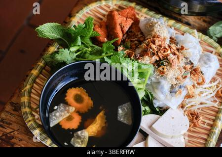 Banh Cuon nach Hanoi-Art, Reisnudelrollen mit gemahlenem Schweinefleisch, serviert mit Cha lua (Wurst), frischen Kräutern und nuoc cham Dipping Sauce im VN Street Foods Stockfoto