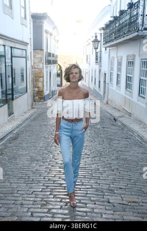 Schöne junge Frau, die auf den Straßen von Faro, Portugal, zur Kamera läuft. Das elegante Modell trägt ein modisches Sommeroutfit. Stockfoto