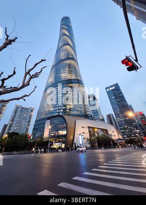 Shanghai, China - 1. April 2025: Blick auf den Shanghai Tower in der Abenddämmerung, umgeben von modernen Wolkenkratzern und Stadtleben an einer geschäftigen Kreuzung in der Innenstadt. Stockfoto