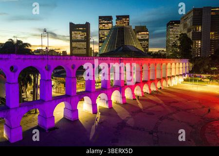 Lapa Aquädukt, beleuchtet mit violetten und rosa Farben am Abend mit hohen Bürogebäuden in der Innenstadt von Rio de Janeiro Stockfoto