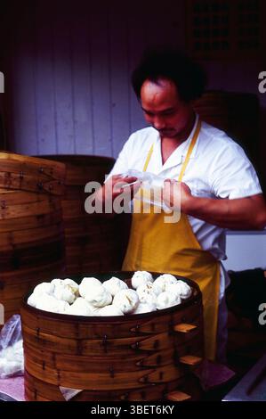 Ein Koch, der von traditionellen Bambusdampfern in einem kleinen Restaurant in Kaifeng, Provinz Henan, China sitzt. Stockfoto