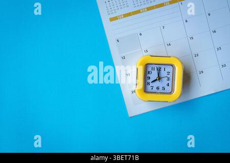 Kalenderseite und gelbe Uhr auf der blauen Tischplatte. Draufsicht, Kopierraum. Stockfoto