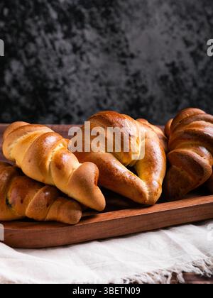 Eine Nahaufnahme mehrerer frisch gebackener Croissants, die auf einem rustikalen Holztablett angeordnet sind. Stockfoto