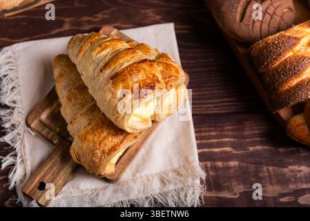 Eine verlockende Auswahl an frisch gebackenem Gebäck, mit cremigem Pudding gefülltem Blätterteig auf einem rustikalen Holzbrett. Stockfoto