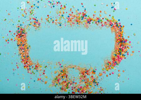 Bunte Streusel und Krümel bilden einen lebendigen Rand um einen leeren, hellblauen Raum, ideal für Text. Stockfoto