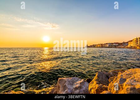 Sonnenuntergang über der adria in Piran, Slowenien. Alte antike und mittelalterliche Stadt, Blick von der Küste und vom Hafen. Alte Steine im Vordergrund, schön Stockfoto