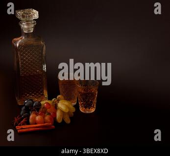 Grappa, Traubenvodka mit Gewürzen in Kristallgläsern auf schwarzem Hintergrund, Trauben verschiedener Sorten in der Nähe. Nahaufnahme. Stockfoto