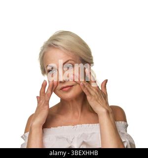 Ältere Frauen massieren die Haut unter den Augen mit den Fingerspitzen vor weißem Hintergrund, reduzieren Schwellungen und unterstützen die Hautpflege mit Selbstvertrauen Stockfoto