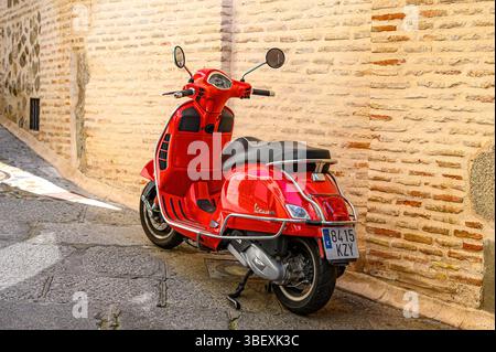 Ein kleines rotes Motorrad parkt in einer engen Straße neben einer mittelalterlichen Backsteinmauer in der Altstadt. Stockfoto