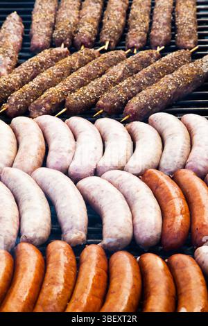 Würstchen und Hackfleisch auf Holzstäbchen werden auf dem Grill gekocht. Stockfoto