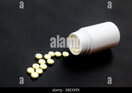 Weißes Plastikglas auf schwarzem Hintergrund mit gegossenen Pillen. Stockfoto