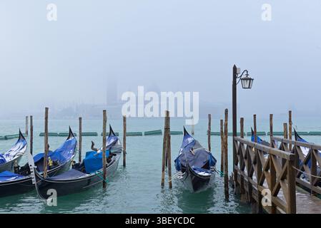 Eine Reihe von Schnee- und frostbedeckten Gondeln in der Nähe des Markusplatzes mit Chiesa di San Giorgio Maggiore im Hintergrund. Venedig, Italien. Stockfoto