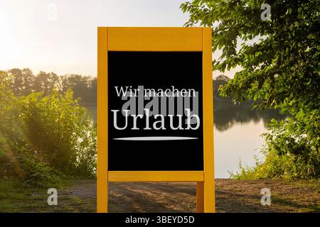 Fotomontage: Stehen Sie mit der Inschrift wir MACHEN URLAUB vor dem Motiv eines Sommerabends am See Stockfoto